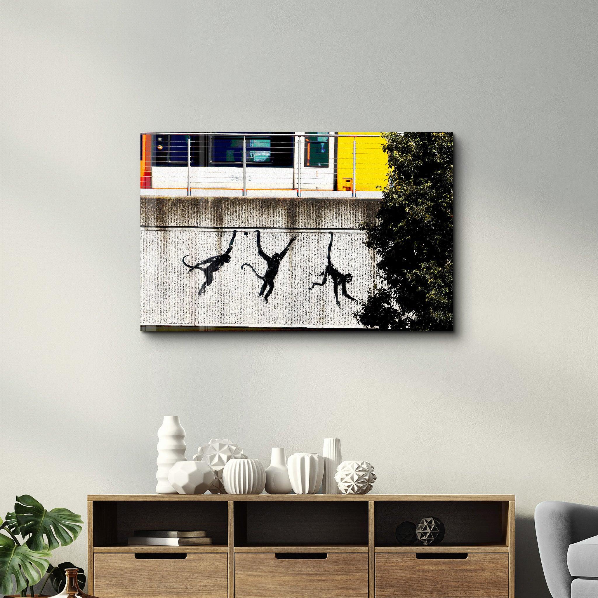 Glass wall art by Artdesigna featuring Banksy's Monkeys on the Train Bridge artwork, displayed on a clear glass panel.